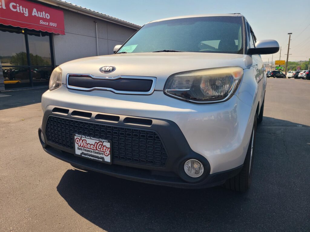 Front view of a silver Kia SUV at a car dealership, Wheel City Auto Finance Centers license plate frame visible on the bumper.