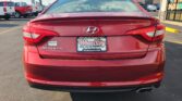 Rear view of a red Hyundai Sonata at a car dealership, license plate reads Wheel City Auto Finance Centers, with other trucks and a showroom on the right.