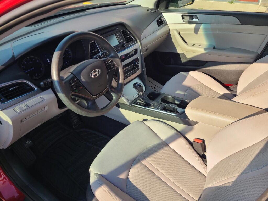 Interior of a car: beige seats, steering wheel, and center console with infotainment screen and controls visible.