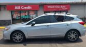 Front of a storefront with red signs reading 'All Credit' and 'Wheel City Auto Since 1993' and a silver SUV parked in front of the shop under a clear blue sky.
