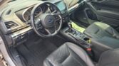 Interior of a modern car cabin showing the driver's seat, steering wheel with a Subaru emblem, and a central touchscreen infotainment system surrounded by control buttons.