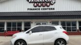 White SUV parked in front of a car dealership building that reads 'Wheel City Auto Finance Centers' with a red bench nearby.