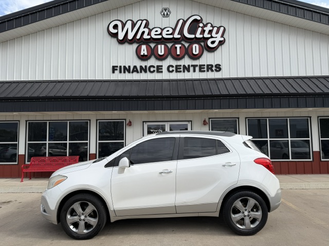 White SUV parked in front of a car dealership building that reads 'Wheel City Auto Finance Centers' with a red bench nearby.