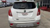 Rear view of a white Buick Encore at a car dealership, showing the dealership plate frame and gray rear bumper with red taillights nearby.