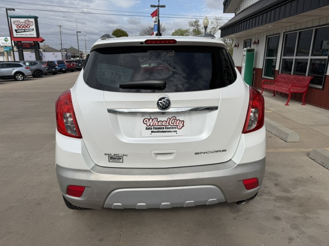 Rear view of a white Buick Encore at a car dealership, showing the dealership plate frame and gray rear bumper with red taillights nearby.