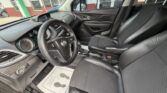 Interior of a car’s front two seats, steering wheel, and dashboard with analog gauges visible, taken from the driver's side door sill.