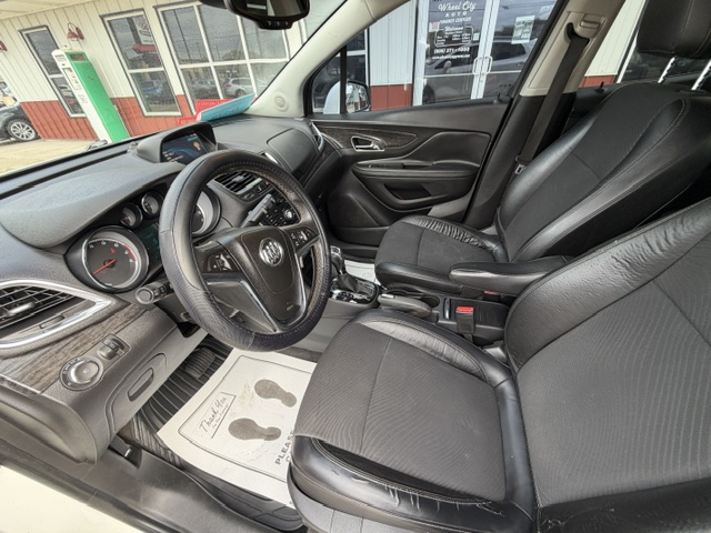 Interior of a car’s front two seats, steering wheel, and dashboard with analog gauges visible, taken from the driver's side door sill.