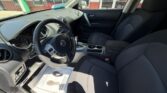 Front interior of a dark-gray car showing the steering wheel, driver and passenger seats, center console with cupholders, and a sunlit dashboard; dealership exterior visible through the windows.