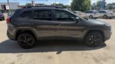 Side view of a dark gray Jeep Grand Cherokee SUV parked in a sunny parking lot with other cars in the background.