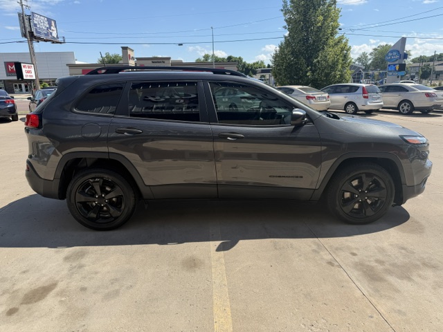 Side view of a dark gray Jeep Grand Cherokee SUV parked in a sunny parking lot with other cars in the background.