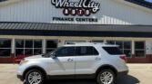 White SUV parked in front of the Wheel City Auto Finance Centers storefront with its sign visible.