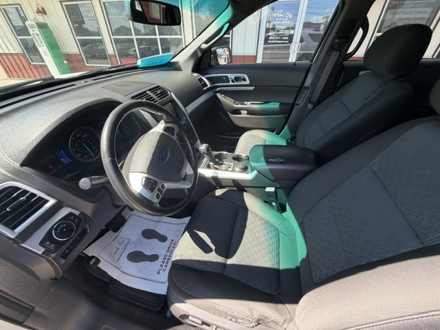 Interior of a dark-gray SUV showing the driver area, steering wheel, center console, and front seats in view at a dealership.