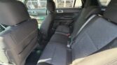 Rear seating area of a car with three black fabric seats and visible seat belts, viewed from the passenger side door fully inside the vehicle.