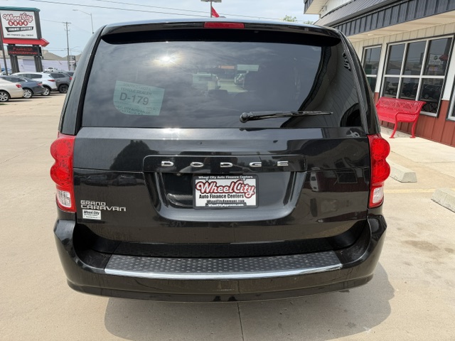 Rear view of a black Dodge Grand Caravan at a dealership, with a Wheel City license plate frame and a silver bumper guard visible under the rear hatch.