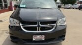 Front view of a black Dodge minivan in a dealership lot, chrome grille with Dodge emblem and Wheel City license frame on the front.
