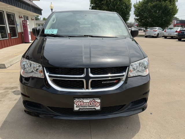 Front view of a black Dodge minivan in a dealership lot, chrome grille with Dodge emblem and Wheel City license frame on the front.
