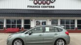 Mint-green hatchback parked in front of Wheel City Auto Finance Centers storefront signs visible above the building front.