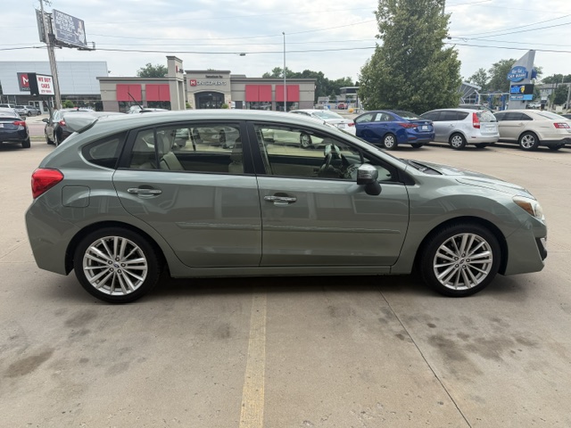 Side view of a gray four-door hatchback car parked in a parking lot with other vehicles and a commercial strip in the background.