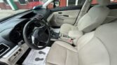 Beige interior of a Subaru sedan, showing driver and front passenger seats, steering wheel, dashboard, and center console with a protective paper floor mat nearby.