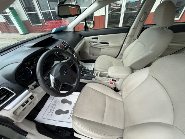 Beige interior of a Subaru sedan, showing driver and front passenger seats, steering wheel, dashboard, and center console with a protective paper floor mat nearby.