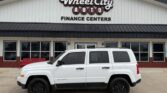 White Jeep Patriot SUV parked in front of Wheel City Auto Finance Centers storefront.