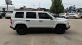 Side view of a white Jeep Patriot SUV parked in a car dealership lot with other vehicles in the background.