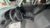 Front interior of a vehicle from the driver's seat, showing steering wheel with a Jeep logo, dashboard, center console, and two gray cloth front seats with a storefront visible outside the windows.