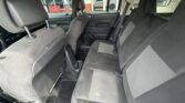 Interior of a car viewed from the rear passenger side, showing a gray fabric back seat with two headrests and a center seatbelt, and the front seats with some wear; overall looks used and slightly dirty.