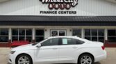 White four-door sedan parked in front of Wheel City Auto Finance Centers storefronts sign on the building