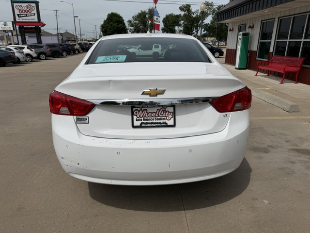 White Chevrolet sedan parked in a dealership lot, rear view with LT badge and Wheel City license plate frame on the dealer plate.