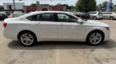 Side view of a white Chevrolet Impala sedan parked in a parking lot near a shopping center.