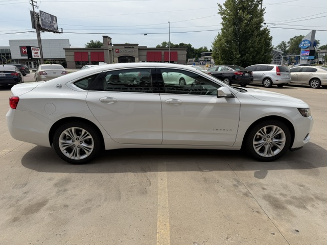 Side view of a white Chevrolet Impala sedan parked in a parking lot near a shopping center.
