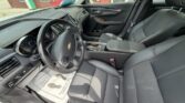 Interior view of a black leather Chevrolet car: steering wheel with emblem, dash, center console, and front seats bathed in natural light.