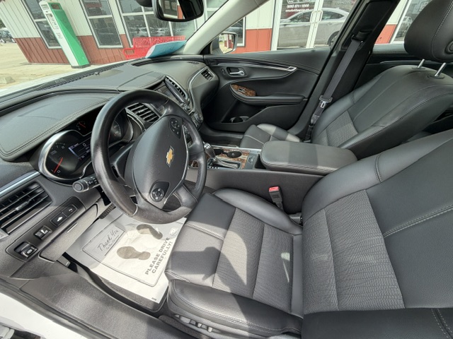 Interior view of a black leather Chevrolet car: steering wheel with emblem, dash, center console, and front seats bathed in natural light.