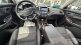 Front interior of a Chevrolet car, view from the back seat showing steering wheel, dashboard touchscreen, and wood-grain center console.