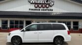 White minivan parked in front of WheelCity Auto Finance Centers storefront on a sunny day.