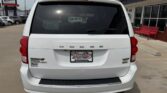Rear view of a white Dodge Grand Caravan in a dealership lot; dealer plate reads Wheel City Auto Finance Center, red taillights, rear wiper, and black bumper step.