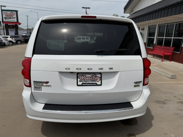 Rear view of a white Dodge Grand Caravan in a dealership lot; dealer plate reads Wheel City Auto Finance Center, red taillights, rear wiper, and black bumper step.