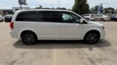 Side view of a white minivan parked in a car dealership lot, featuring dark-tinted windows and black alloy wheels.