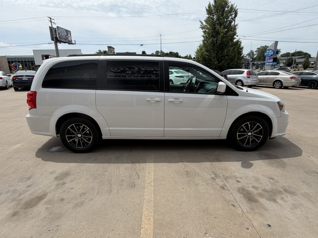 Side view of a white minivan parked in a car dealership lot, featuring dark-tinted windows and black alloy wheels.