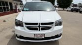 Front view of a white Dodge minivan in a dealership lot, Wheel City license plate frame visible.