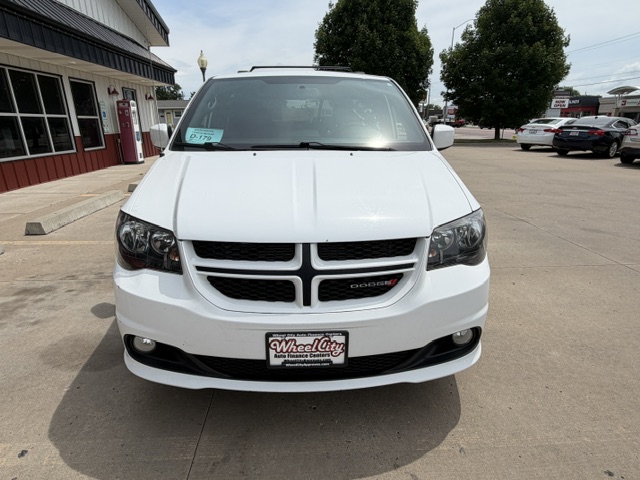 Front view of a white Dodge minivan in a dealership lot, Wheel City license plate frame visible.