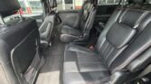 Inside a black leather SUV with two captain chairs in the middle row and a rear bench, red stitching.