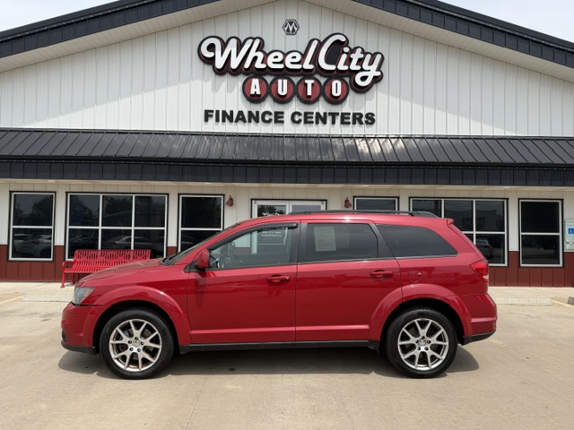 Red SUV parked in front of Wheel City Auto Finance Centers storefront with beige building and large sign above the entrance.