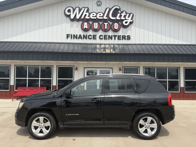 Black Chevrolet Compass SUV parked in front of Wheel City Auto Finance Centers storefront, with a red bench visible to the left.