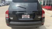 Rear view of a black Jeep SUV (4x4) parked in a dealership lot; license plate frame reads Wheel City Auto Finance Centers, with red benches and storefront in background.