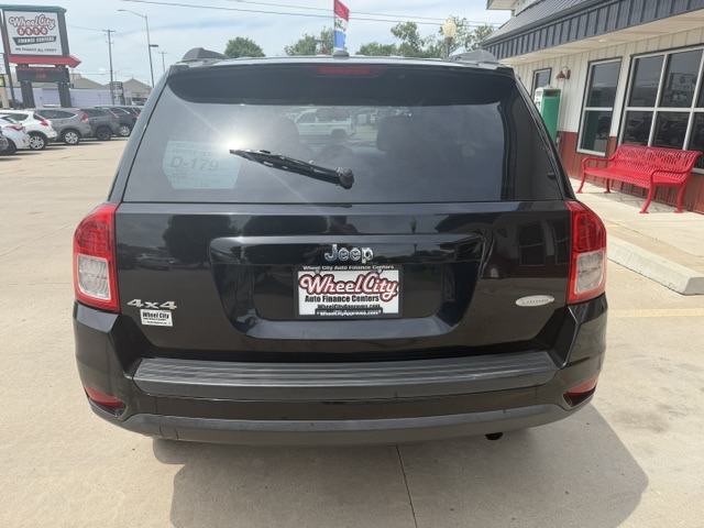 Rear view of a black Jeep SUV (4x4) parked in a dealership lot; license plate frame reads Wheel City Auto Finance Centers, with red benches and storefront in background.