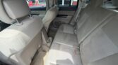 Rear passenger area of a beige cloth-upholstered SUV, with headrests, seat belts, and a cup holder on the floor between seats.