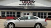 Silver sedan parked in front of a Wheel City Auto Finance Centers building; dealership sign visible above the entrance