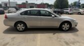 Silver four-door sedan photographed in a parking lot, with storefronts and other parked cars in the background.